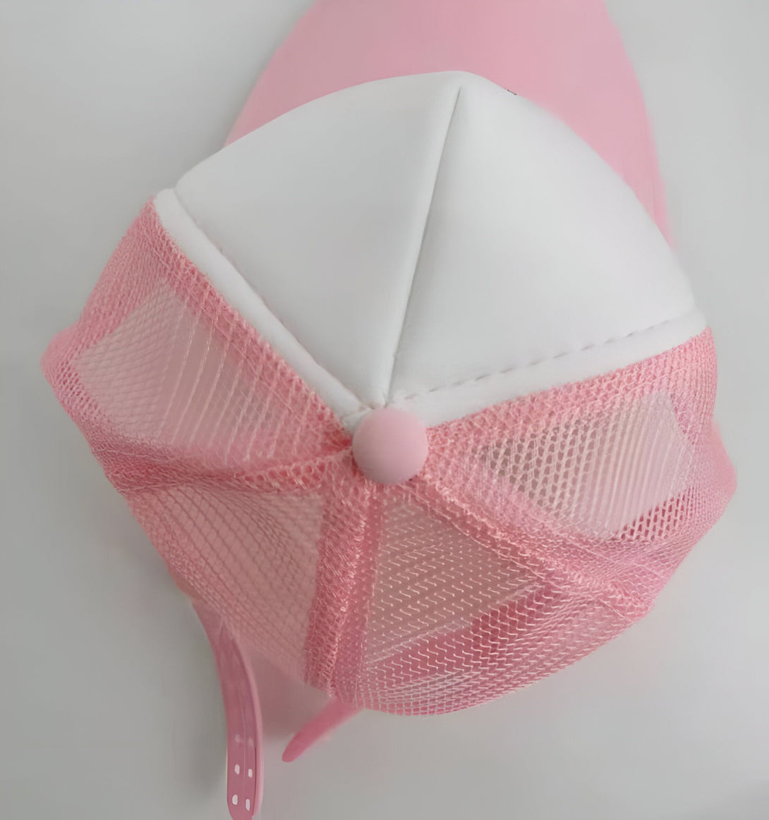 Une casquette rose avec un filet blanc à l'arrière. La visière est blanche et il y a un bouton rose sur le dessus de la casquette.