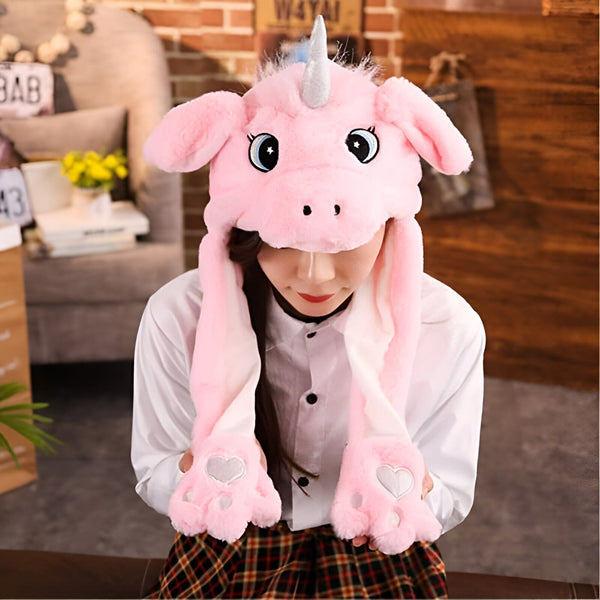 Une femme portant un bonnet rose en forme de licorne avec des oreilles pendantes. Le bonnet a des yeux de dessin animé, une corne argentée et des gants intégrés en forme de pattes avec des cœurs. Elle porte une chemise blanche et une jupe à carreaux rouge., 45502402724095 | Licorne Shop