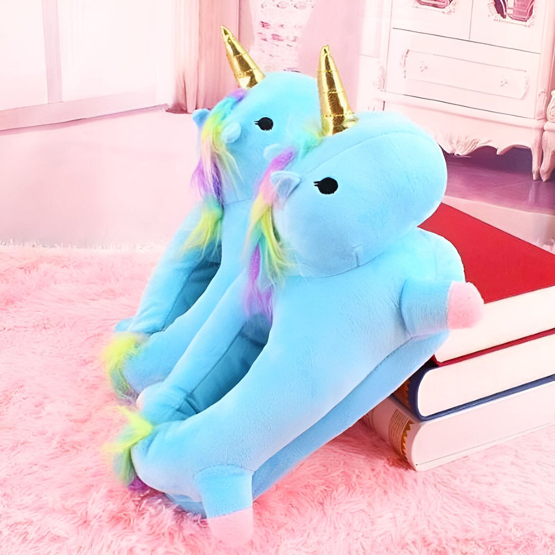 Une paire de pantoufles licorne en peluche bleue avec une corne dorée et une crinière arc-en-ciel.