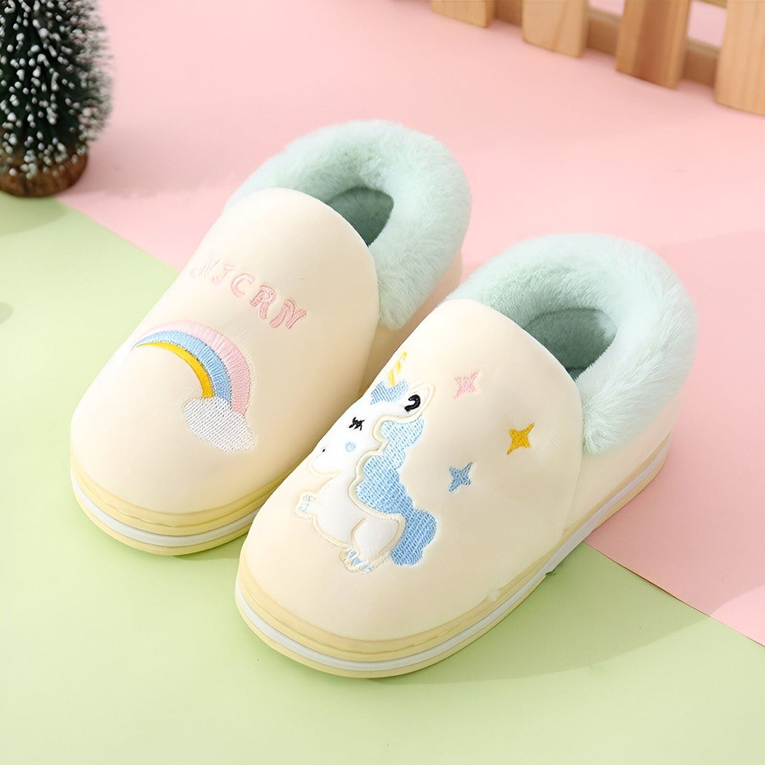 Une paire de pantoufles licorne en peluche avec une fourrure verte à l'intérieur. Les pantoufles sont jaunes avec un arc-en-ciel et une licorne brodés dessus.