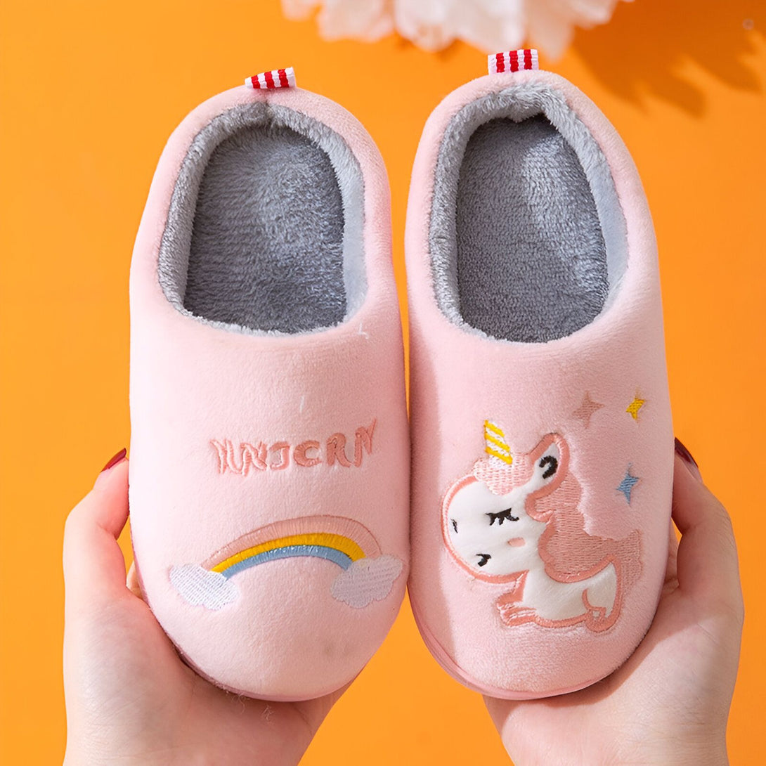 Une paire de pantoufles roses pour enfant avec une licorne brodée dessus. Les pantoufles sont doublées de fourrure grise.