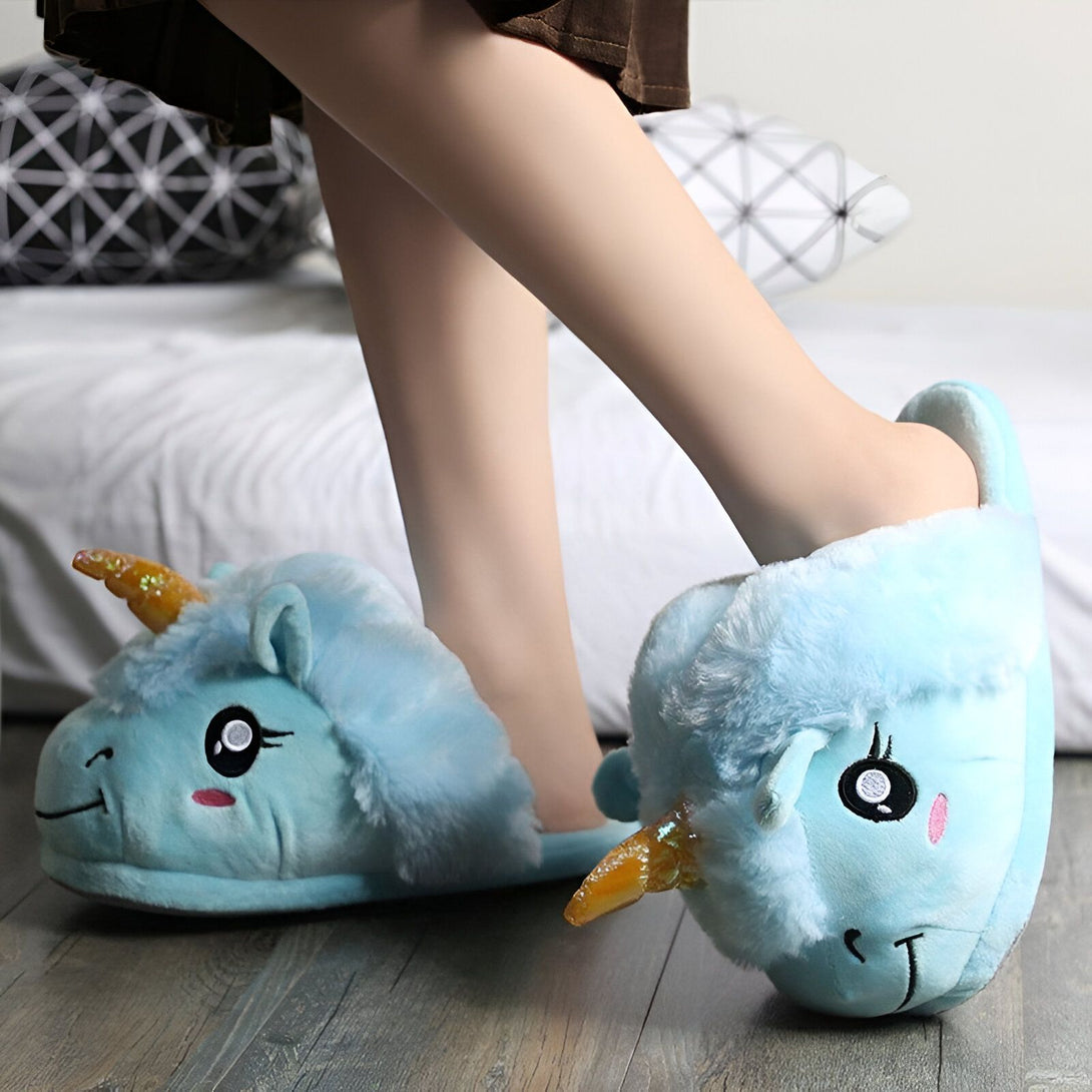 Une paire de pantoufles licorne en peluche bleue avec une corne dorée et un visage souriant.