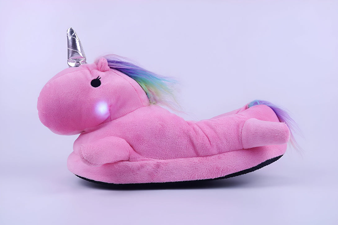 Une peluche licorne rose avec une corne argentée et une crinière arc-en-ciel. La peluche est éclairée par une lumière rose.