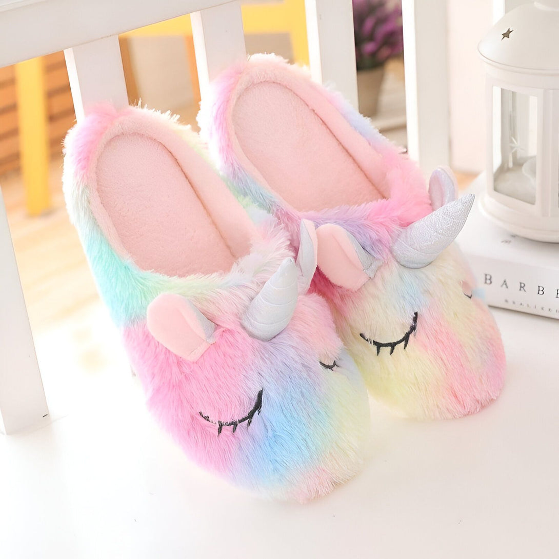 Une paire de pantoufles licorne en peluche arc-en-ciel avec des yeux fermés et une corne argentée.