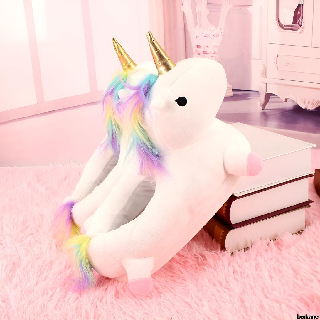 Une peluche licorne blanche avec une corne dorée et une crinière arc-en-ciel. Elle est posée sur un tapis rose à côté d'une pile de livres.