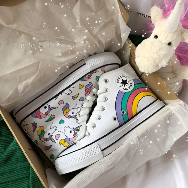 Paire de baskets montantes blanches dans une boîte. Une basket a un motif d'unicorne, l'autre a un arc-en-ciel et un logo "All Star". Un jouet en forme d'unicorne se trouve également dans la boîte., 45502173937919,45502173970687,45502174003455,45502174036223,45502174068991,45502174101759,45502174134527,45502174167295,45502174200063 | Licorne Shop