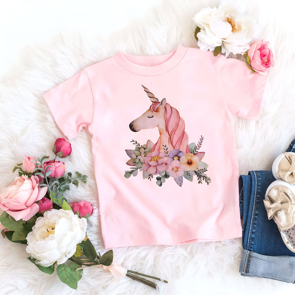 T-shirt rose clair pour enfant avec dessin de tête de licorne entourée de fleurs, posé sur une fourrure blanche, accompagné de fleurs roses et blanches, d'un jean et de chaussures dorées., 45502317854975,45502317887743,45502317920511,45502317953279,45502317986047,45502318018815,45502318051583,45502318084351 | Licorne Shop