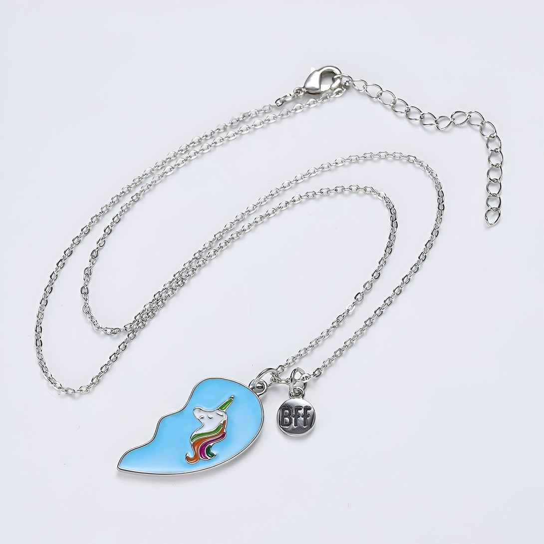 Deux moitiés de pendentif en forme de cœur avec une chaîne en argent. Les pendentifs sont bleus avec une licorne blanche et arc-en-ciel. Il y a un petit pendentif en forme de cœur avec les lettres BFF.