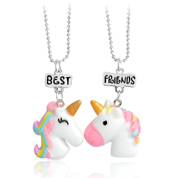 Deux pendentifs en forme de licorne blanche avec des crinières arc-en-ciel et des cornes dorées. Les pendentifs sont attachés à des chaînes en argent et comportent des breloques avec les mots "Best Friends".