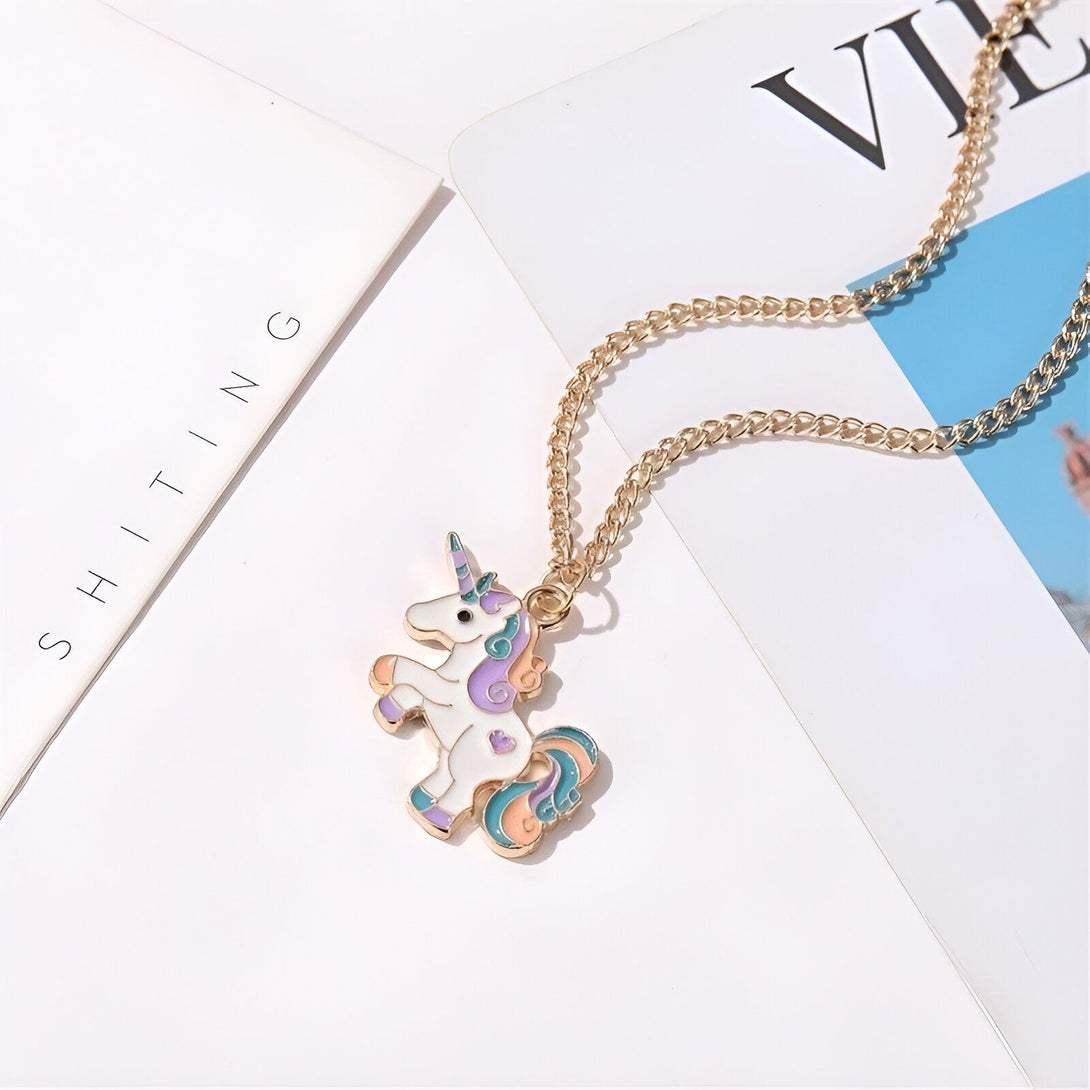 L'image représente un collier avec un pendentif en forme de licorne. La licorne est blanche avec une crinière et une queue arc-en-ciel. Le collier est en métal doré.