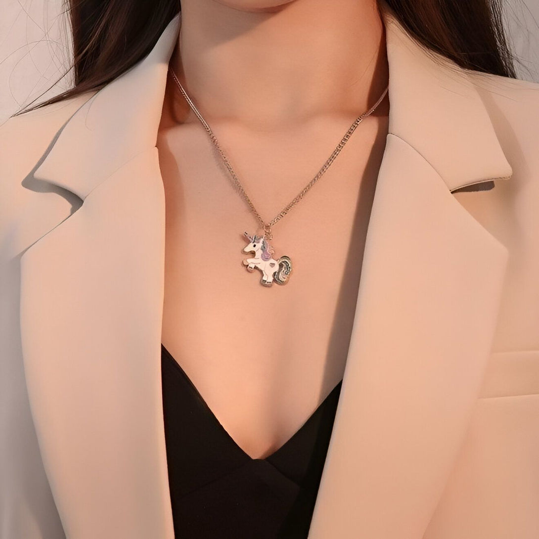 Une jeune femme porte un collier avec un pendentif licorne. La licorne est blanche avec une crinière et une queue arc-en-ciel. Le collier est en métal doré.