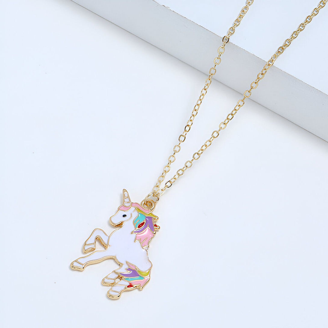 L'image représente un collier avec un pendentif en forme de licorne. La licorne est blanche avec une crinière et une queue arc-en-ciel. Le collier est en métal doré.