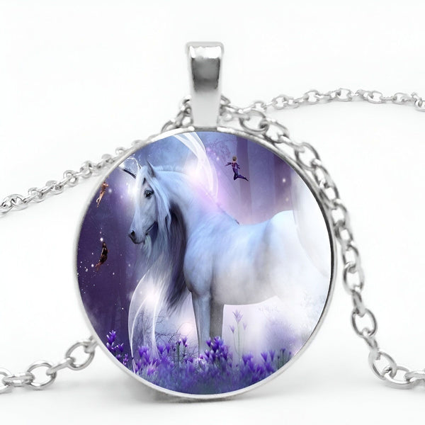 Un pendentif en forme de licorne blanche avec des ailes et une crinière violettes. La licorne est entourée de fleurs violettes et de fées. Le pendentif est en métal argenté et est suspendu à une chaîne en métal argenté.