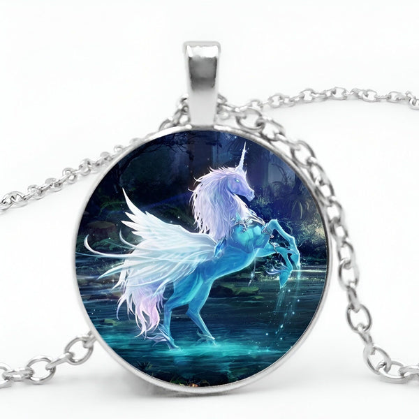 L'image représente un pendentif en forme de cercle avec une chaîne en argent. Le pendentif représente une licorne blanche avec des ailes bleues et une crinière rose. La licorne se tient sur un fond bleu avec des arbres et des étoiles.