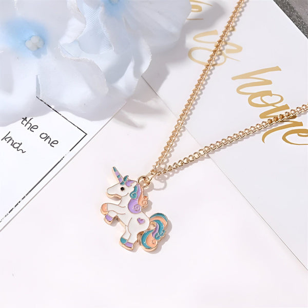 L'image représente un collier avec un pendentif en forme de licorne. La licorne est blanche avec une crinière et une queue arc-en-ciel. Le collier est en métal doré.