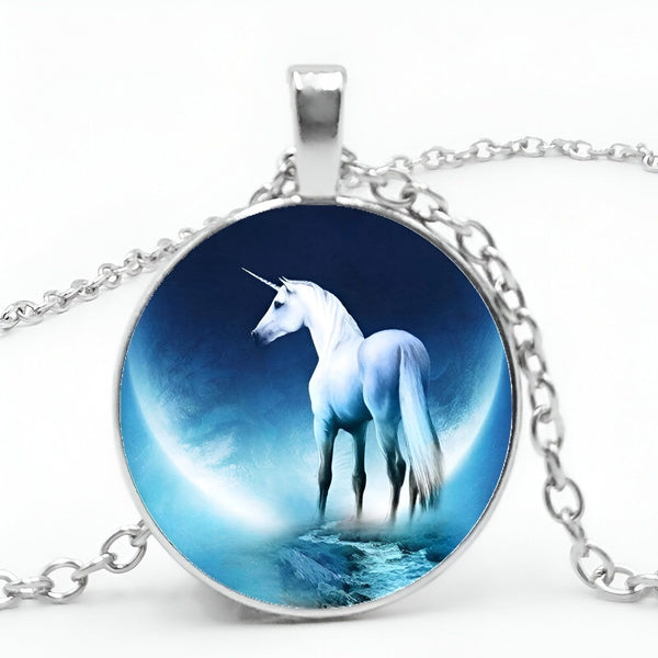 Un pendentif en forme de licorne blanche avec une crinière et une queue bleues. La licorne se tient sur un croissant de lune et est entourée d'étoiles. Le pendentif est en métal argenté et est suspendu à une chaîne en métal argenté.