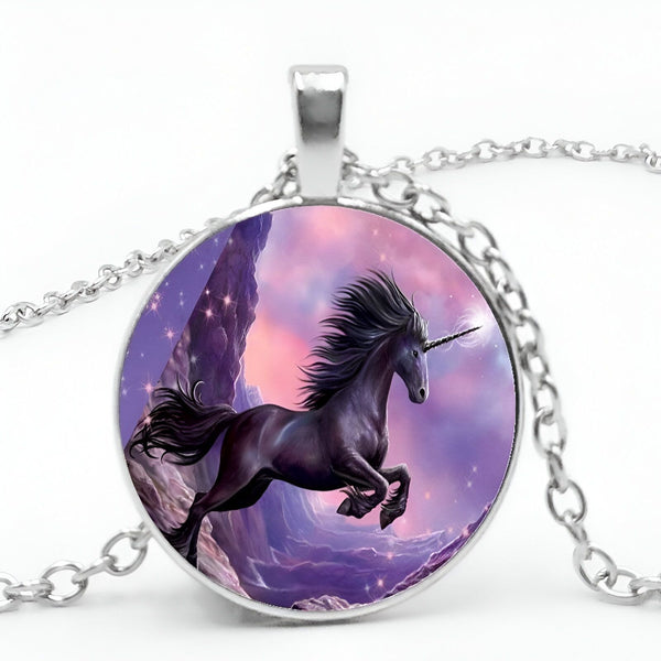 Un pendentif en forme de cercle avec une image d'une licorne noire. La licorne est représentée avec une crinière et une queue noires, et un corps blanc. Elle se tient sur un fond de ciel violet et de montagnes. Le pendentif est en métal argenté et est suspendu à une chaîne en métal argenté.