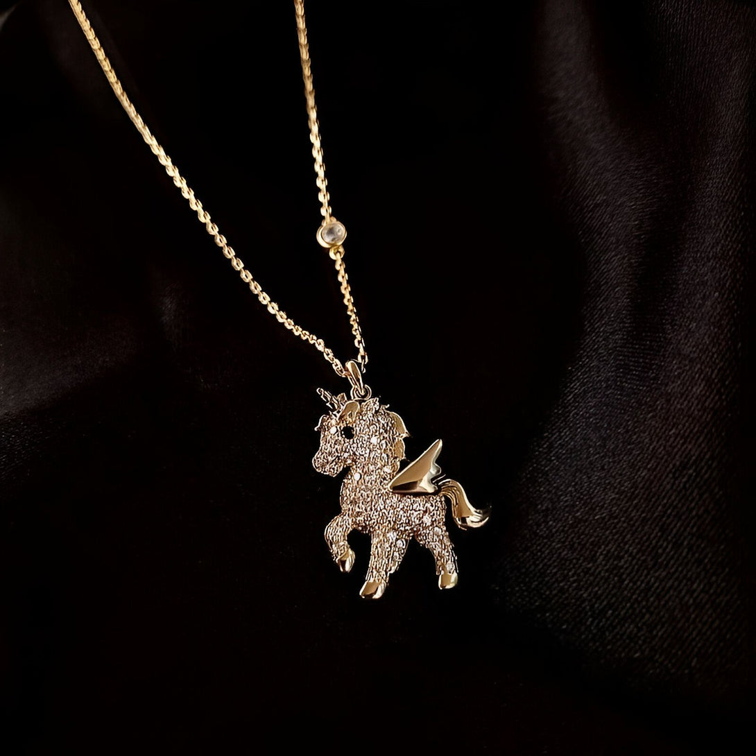 Un pendentif en forme de licorne en or avec des ailes et des pierres précieuses sur un fond noir.
