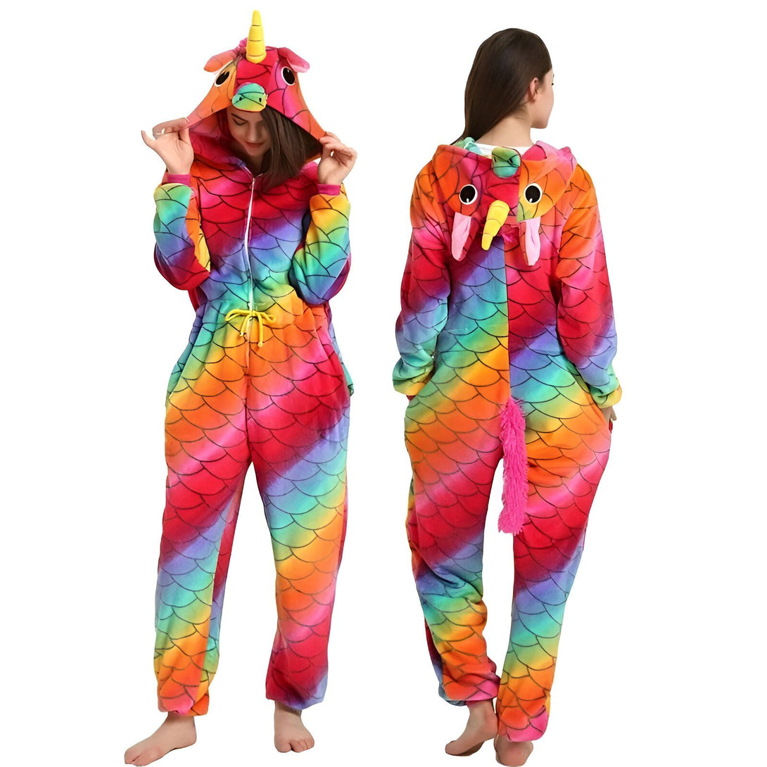 Une femme porte une combinaison pyjama licorne arc-en-ciel avec une capuche. La combinaison est rose, jaune, verte, bleue et violette. La capuche a une corne de licorne et des oreilles de licorne. La combinaison est zippée sur le devant. La femme est pieds nus.