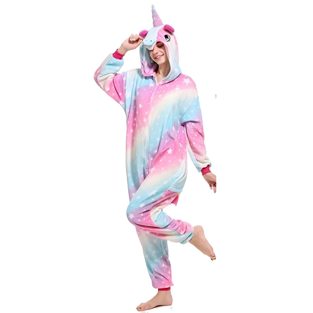 Une femme porte un pyjama licorne rose et bleu avec une capuche. Le pyjama est en matière peluche et a des étoiles et des lunes imprimées. La femme est debout et a les pieds nus.