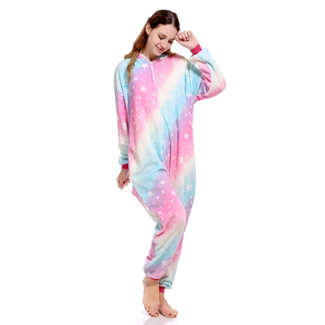 Une femme porte une combinaison pyjama licorne arc-en-ciel avec des étoiles blanches. Elle est souriante et a les cheveux longs.