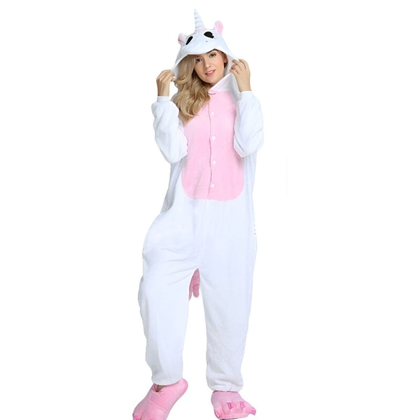 Une femme porte une combinaison pyjama licorne blanche et rose. La combinaison est à capuche et a des détails en peluche. La femme est debout et regarde l'appareil photo.