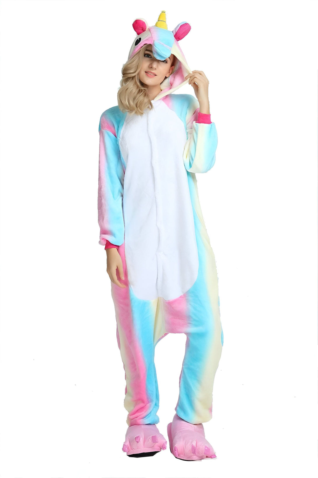 Une femme porte une combinaison pyjama licorne arc-en-ciel avec une capuche. La combinaison est rose, bleue et blanche. La femme a les cheveux blonds et elle sourit.
