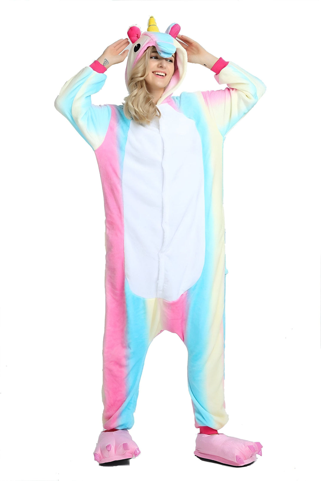Une femme porte un pyjama licorne arc-en-ciel. Le pyjama est rose, bleu et jaune avec une capuche licorne. La femme est heureuse et sourit.