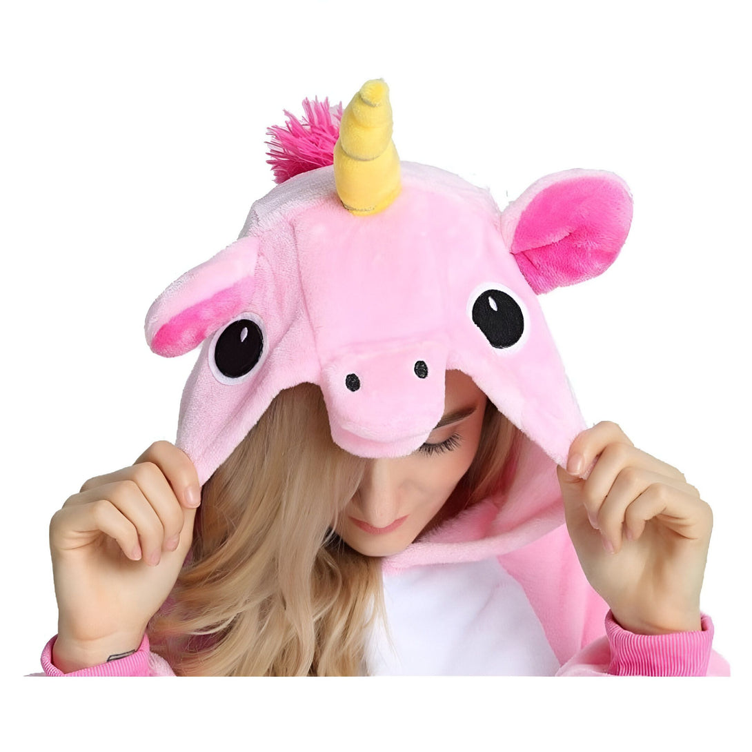 Une femme porte une combinaison pyjama licorne rose avec une capuche. La capuche a une corne de licorne jaune et des oreilles roses. La combinaison est ouverte au niveau du cou et l'on peut voir le visage de la femme. Elle a les cheveux blonds et sourit.