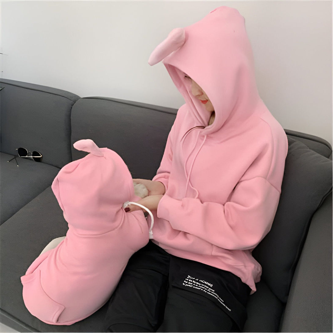 Une femme assise sur un canapé gris porte un sweat à capuche rose avec des oreilles de lapin. Un chien est assis devant elle et porte un sweat à capuche rose assorti., 45501215375615,45501215408383,45501215441151,45501215473919,45501215506687,45501215539455,45501215572223,45501215604991 | Licorne Shop