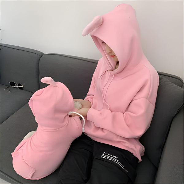 Une femme assise sur un canapé gris porte un sweat à capuche rose avec des oreilles de lapin. Un chien est assis devant elle et porte un sweat à capuche rose assorti., 45501215375615,45501215408383,45501215441151,45501215473919,45501215506687,45501215539455,45501215572223,45501215604991 | Licorne Shop