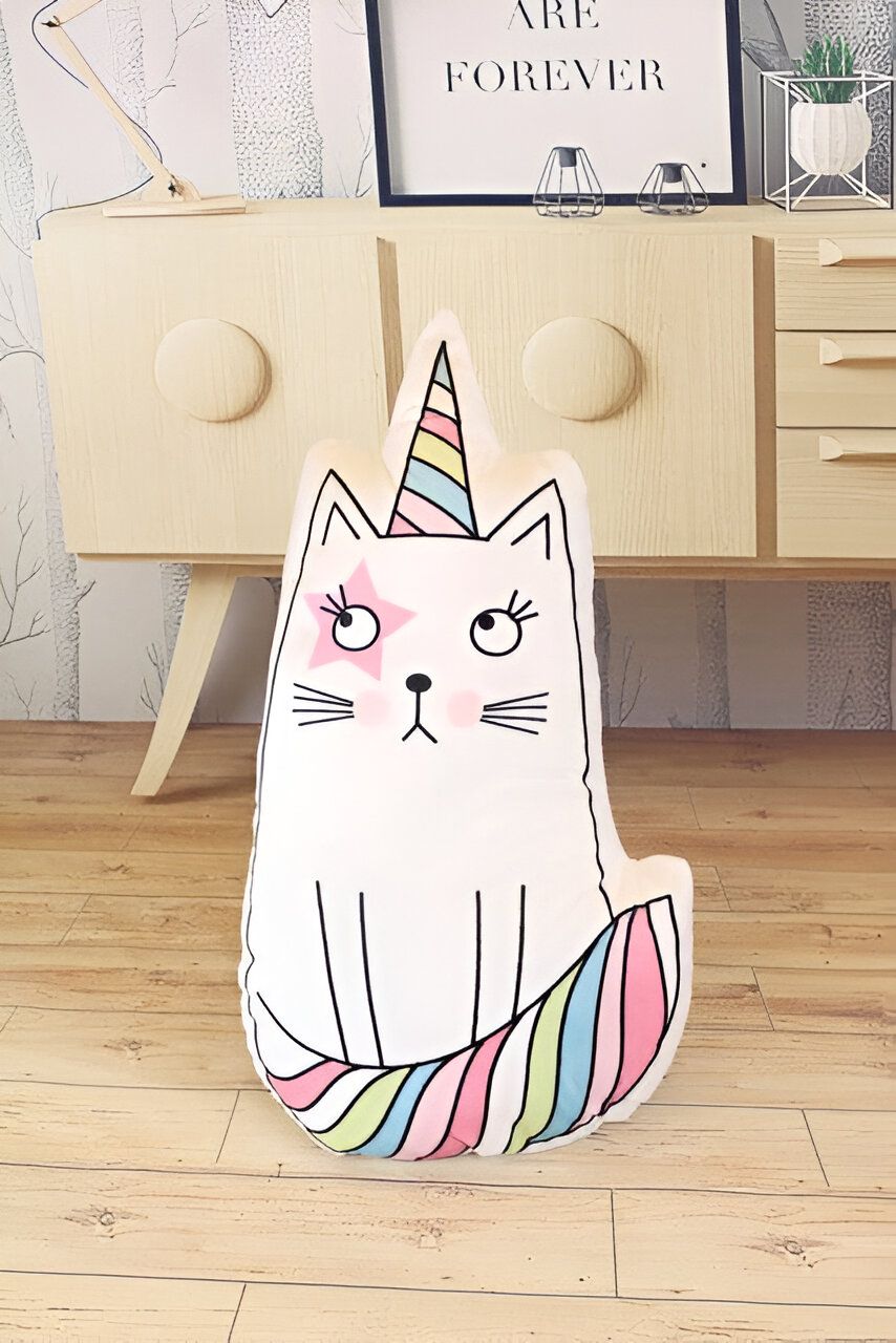 Coussin décoratif en forme de chat licorne blanc avec une étoile rose sur l'œil, une corne rayée multicolore et une queue assortie, posé devant un buffet en bois clair dans une chambre d'enfant., 45501065167103 | Licorne Shop