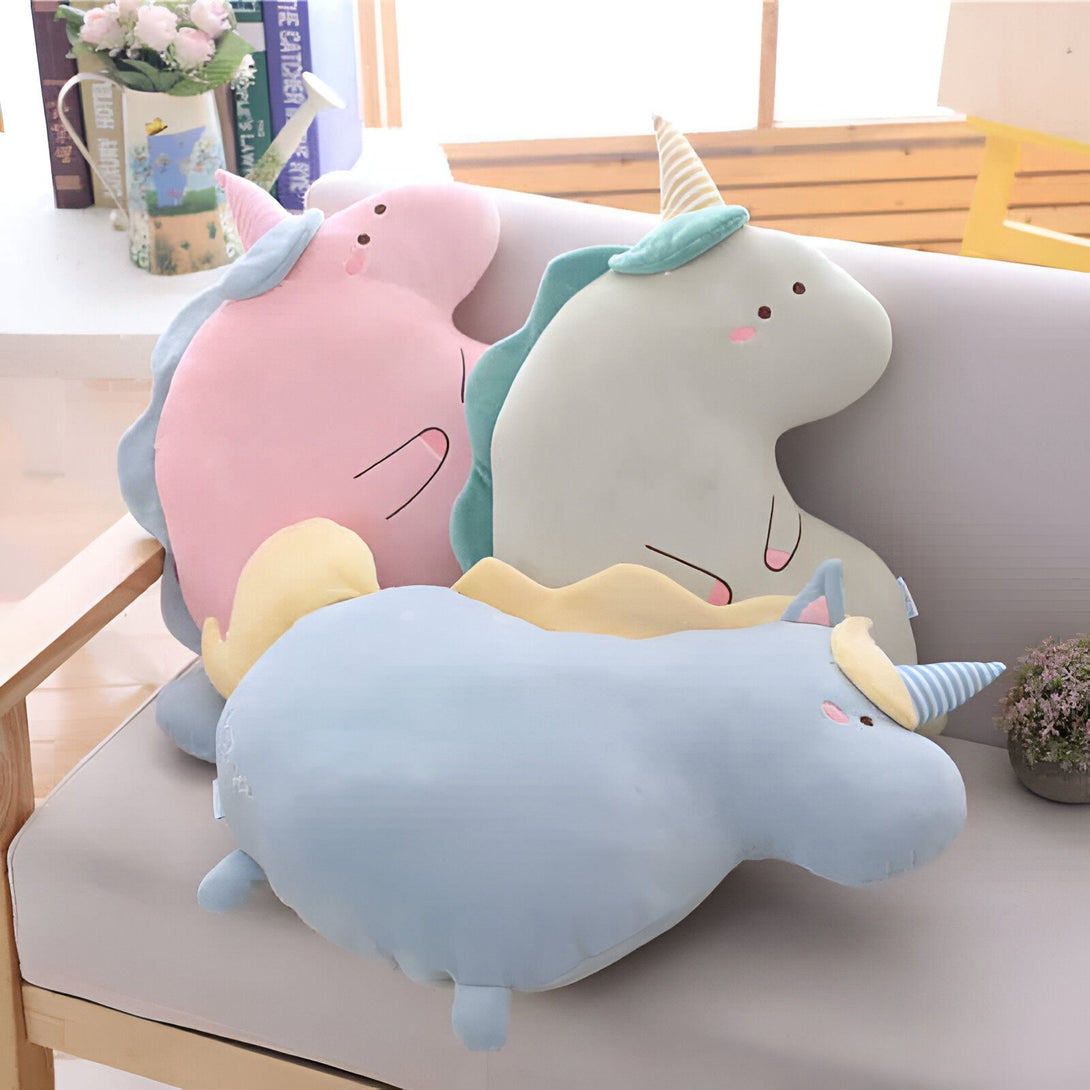 Trois coussins en forme de licorne dans les tons pastel rose, blanc et bleu, posés sur un canapé. Une plante et des livres sont visibles en arrière-plan., 45501061988607 | Licorne Shop