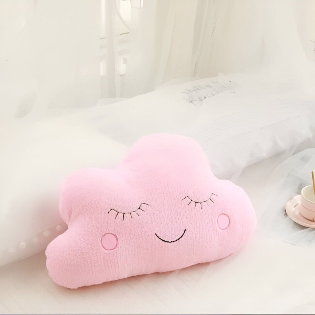 Coussin décoratif rose en forme de nuage avec un visage souriant et les yeux fermés, posé sur un lit blanc. Accessoire de chambre d'enfant., 45501065756927 | Licorne Shop