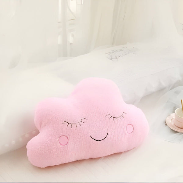 Coussin décoratif rose en forme de nuage avec un visage souriant et les yeux fermés, posé sur un lit blanc. Accessoire de chambre d'enfant., 45501065756927 | Licorne Shop