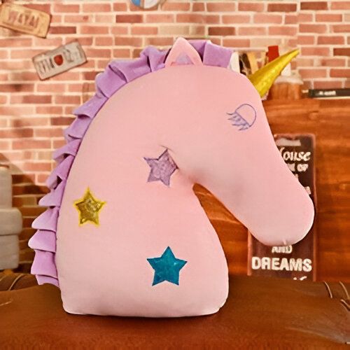 Coussin décoratif en forme de licorne rose avec des étoiles et une crinière lavande. Un fond de briques ajoute une ambiance chaleureuse et ludique à la photo, idéal pour une chambre d'enfant. L'image met en valeur un accessoire mignon et confortable., 45501049307391 | Licorne Shop