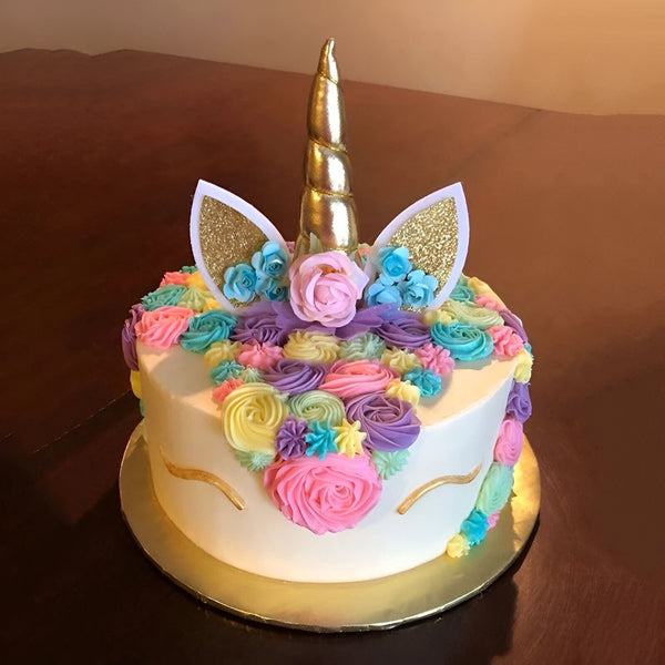 Une image d'un gâteau licorne avec une corne dorée, des oreilles et des fleurs en pâte à sucre colorée.