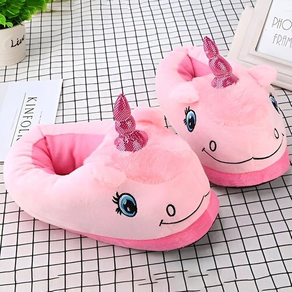 Image de deux pantoufles roses en forme de licorne avec une corne brillante, posées sur un tissu à carreaux. Un pot de plante et un cadre photo sont visibles en arrière-plan., 45502271095039,45502271127807,45502271160575,45502271193343,45502271226111,45502271258879,45502271291647,45502271324415,45502271357183 | Licorne Shop
