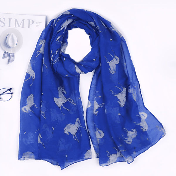 Écharpe bleu roi à motifs de chevaux argentés, posée à plat près d'un chapeau, de lunettes et d'un magazine. Accessoire de mode élégant et tendance pour femme., 45502083825919 | Licorne Shop