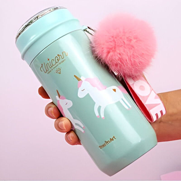 Gourde turquoise avec motif licornes blanches et pompon rose, tenue par une main. Idéale pour les enfants et les adultes fans de licornes. Accessoire mignon et pratique pour rester hydraté avec style., 45501171761407 | Licorne Shop
