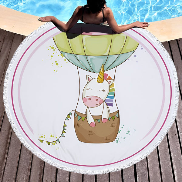 Serviette de plage ronde avec dessin d'une licorne dans une montgolfière, posée près d'une piscine. Une personne est allongée à côté de la serviette., 45501254533375 | Licorne Shop