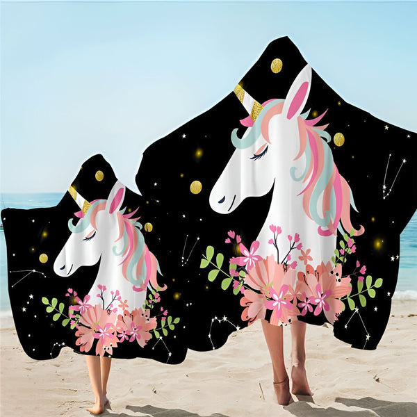 Deux personnes à la plage portent des couvertures à capuche décorées de motifs d'unicorne, de fleurs et d'étoiles. Le fond est noir avec des touches dorées., 45501225697535 | Licorne Shop