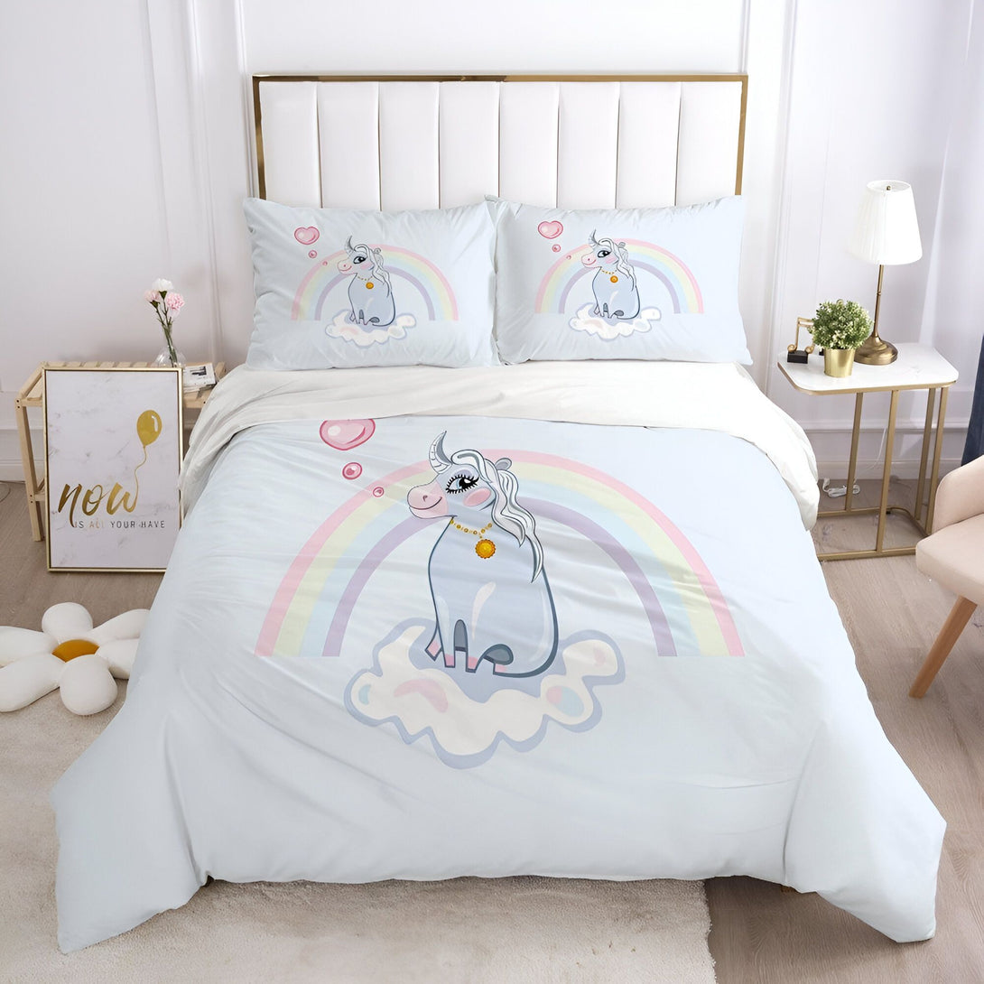 Une chambre avec une parure de lit licorne. La parure de lit est composée d'une housse de couette et de deux taies d'oreiller. La housse de couette est imprimée d'une licorne assise sur un nuage. La licorne est entourée d'un arc-en-ciel et de bulles. Les taies d'oreiller sont imprimées de la même licorne. La parure de lit est en coton et est lavable en machine.