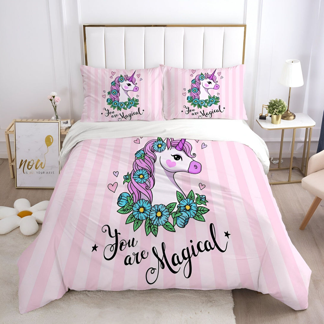 Une couette rose à rayures blanches avec une licorne blanche et des fleurs bleues. Il est écrit "You are magical" (Tu es magique) sur la couette.