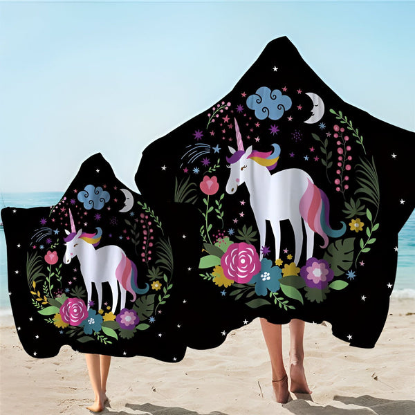 Deux personnes sur la plage portant des serviettes à capuche noires avec un motif de licorne blanche, des fleurs colorées, des étoiles, un croissant de lune et des nuages. Idéal pour les enfants et les adultes après la baignade., 45501226090751 | Licorne Shop