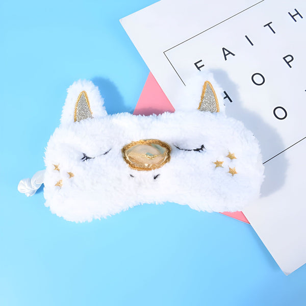 Masque de sommeil blanc en fausse fourrure en forme de licorne, avec des détails dorés sur les oreilles, la corne et des petites étoiles. Il repose sur un fond bleu clair à côté d'un papier blanc et rose., 45501058154751 | Licorne Shop