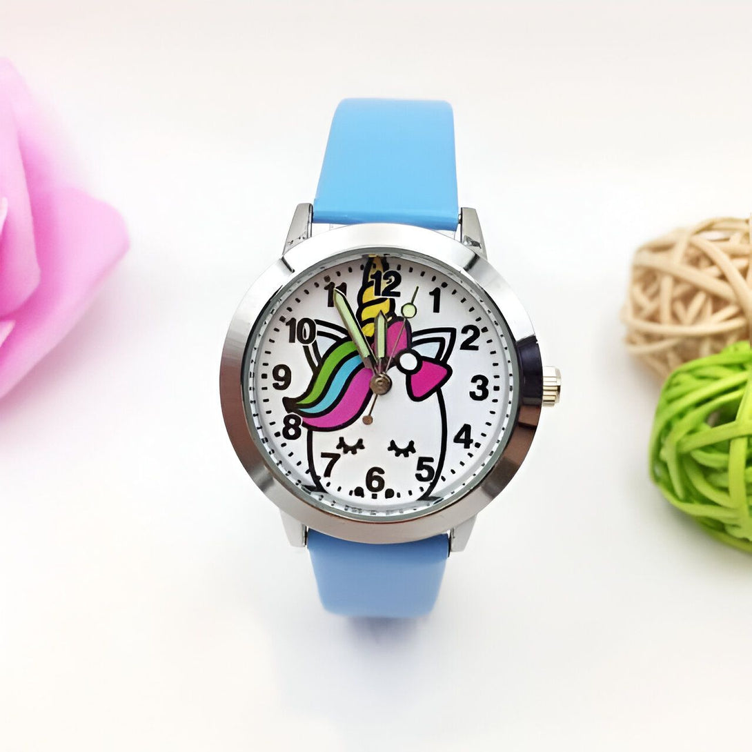 Montre pour enfant avec un bracelet bleu clair. Le cadran de la montre représente une licorne blanche avec une crinière arc-en-ciel et un nœud rose. Les chiffres sont clairement visibles sur le cadran., 45501128737023 | Licorne Shop