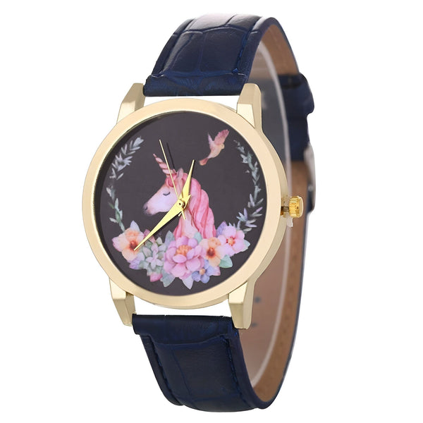 Une montre avec un cadran rond et un bracelet en cuir bleu. Le cadran est noir avec une image d'une licorne blanche et rose avec des fleurs et des oiseaux.