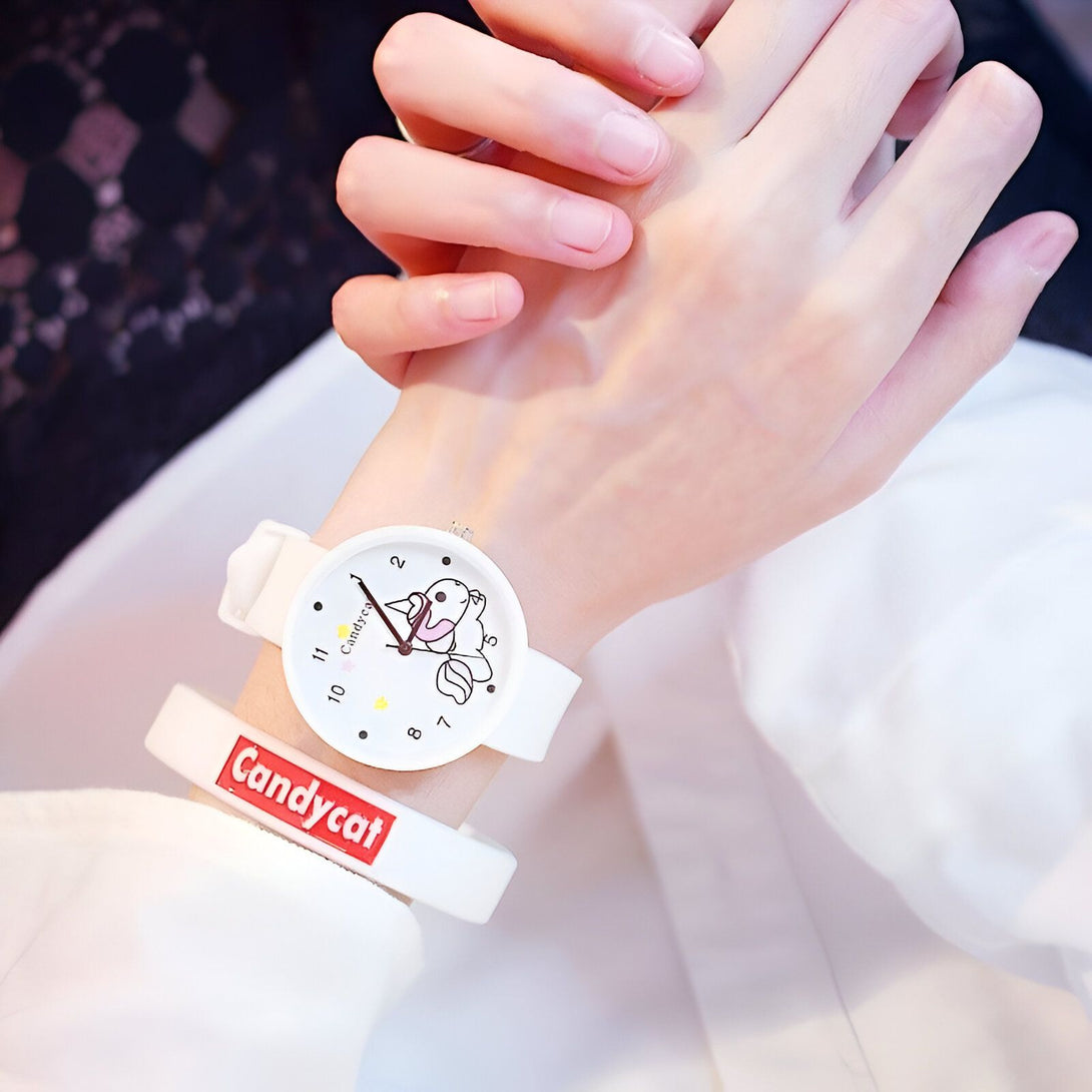 Une jeune fille porte une montre blanche avec un bracelet en silicone blanc. Le cadran de la montre est rond et blanc avec des chiffres noirs. Il y a un petit dessin d'un chat sur le cadran. Le bracelet de la montre est en silicone blanc avec le logo "Candycat" écrit en rouge.