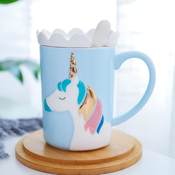 Image d'un joli mug bleu clair décoré d'un dessin de licorne blanche avec crinière colorée et corne dorée. Le mug repose sur un sous-tasse en bois et a un couvercle blanc avec une cuillère assortie., 45501196108031 | Licorne Shop